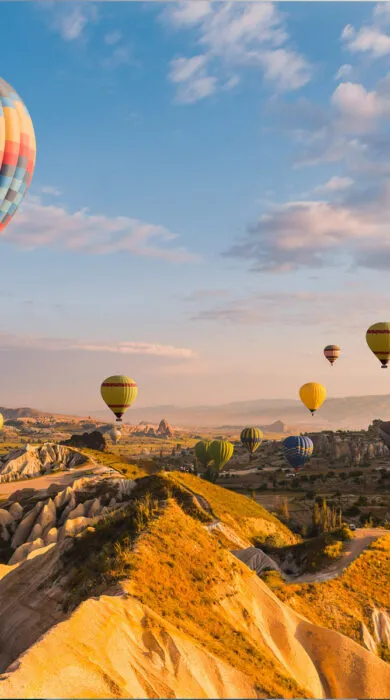 Colorful hot air balloons floating over scenic landscape during sunrise or sunset