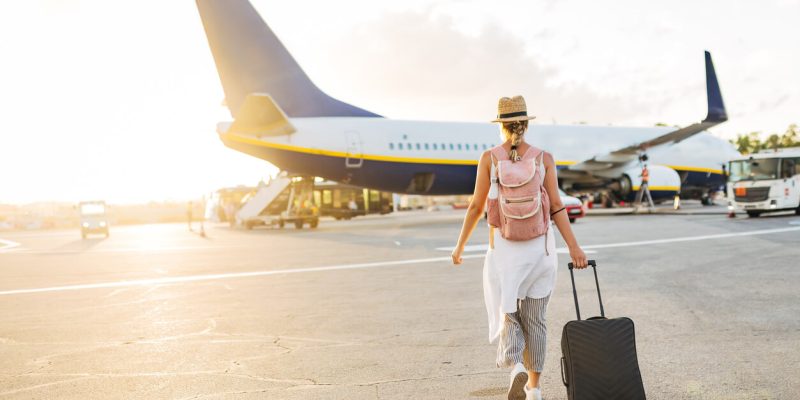 Female traveler walking toward airplane at sunset — vacation departure, summer 2025 travel, and global travel planning.
