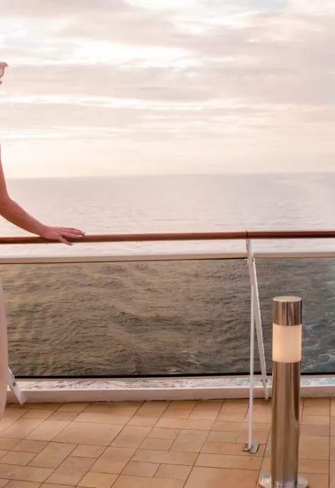 Woman in a sunhat and dress gazing at the ocean from a luxury cruise ship balcony at sunset
