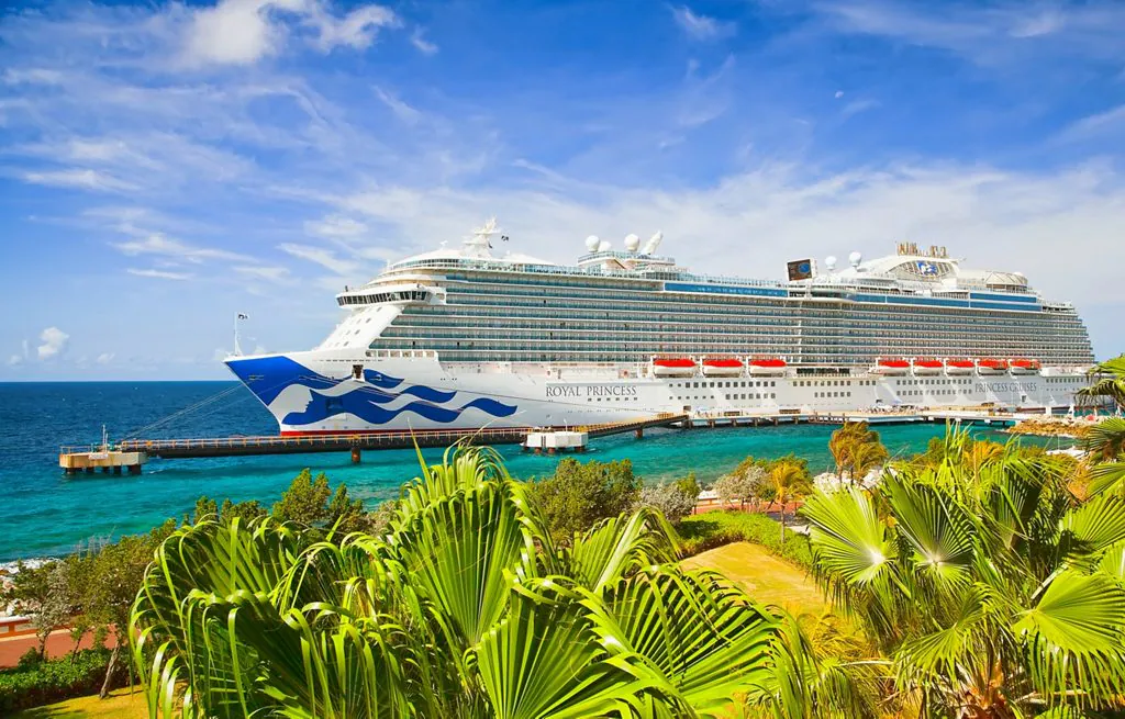 Royal Princess cruise ship docked in the Caribbean surrounded by turquoise waters and tropical palm trees under a bright blue sky