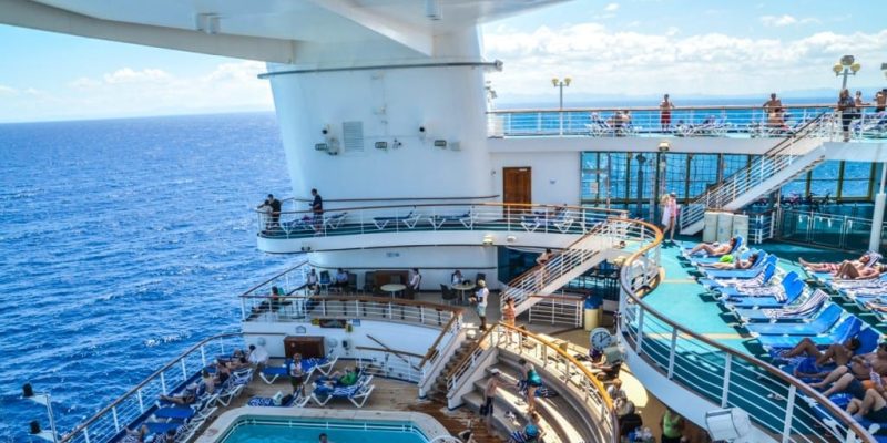 Guests relaxing by the pool aboard a Caribbean Princess cruise ship with panoramic ocean views under a clear blue sky