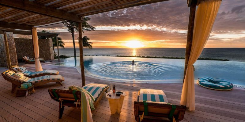 Luxury beachfront resort with infinity pool overlooking the ocean at sunset, featuring cabanas and lounge chairs for Regent Seven Seas guests